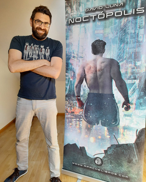 David Luna posando junto a un cartel promocional de Noctópolis